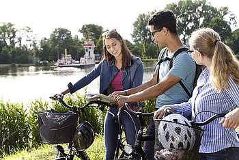 Drei Fahrradfahrer stehen am Kanal und suchen im Plan nach einer Fahrradroute